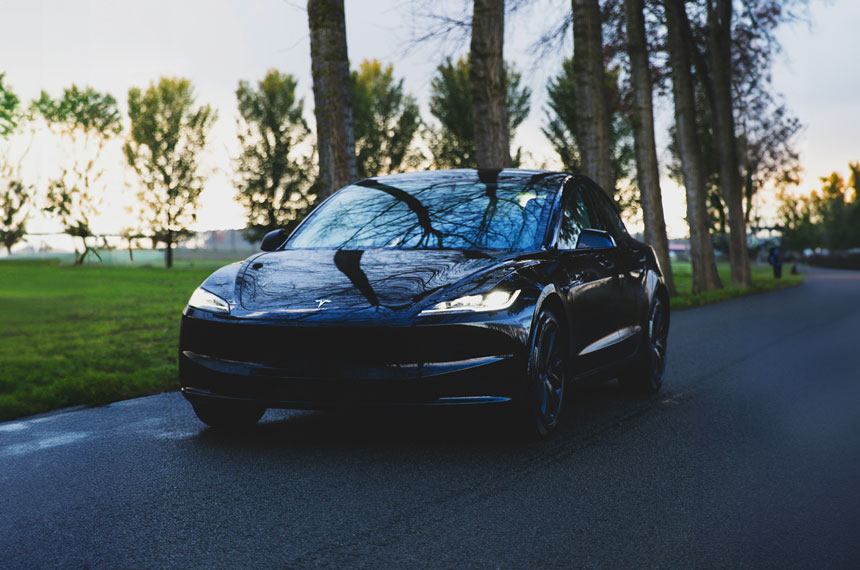 Автомобиль Tesla движется по дороге, по сторонам которй растут деревья